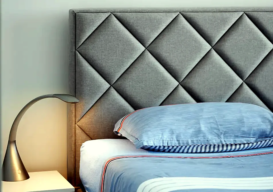 A grey headboard with a bedside lamp